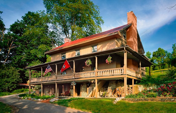 A two-story Hawley house farmhouse with a red metal roof, a wide wooden porch, and American and Tennessee state flags hanging from the railing.