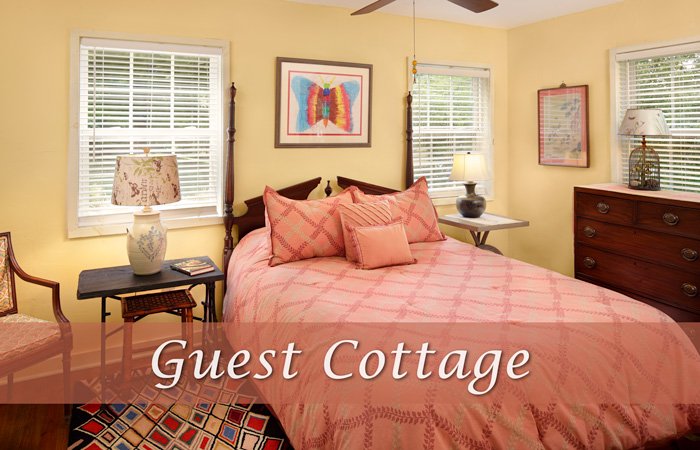 A Hawley House bedroom with yellow walls, a four-poster bed with a coral patterned quilt, and two side tables with lamps, overlaid with the text “Guest Cottage.”
