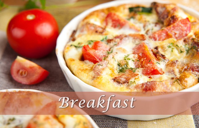 A small quiche with tomato and herbs in a white dish at Hawley House, next to a fresh tomato, with the word “Breakfast” overlaid.